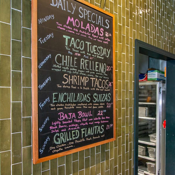 A Miguelito's Cocina Mexicana chalkboard menu displays daily specials against a green tiled wall.