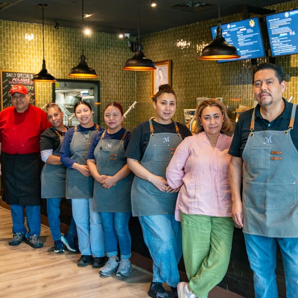 Miguelito's Cocina Mexicana staff, seven people in aprons, standing in front of a green tiled wall.