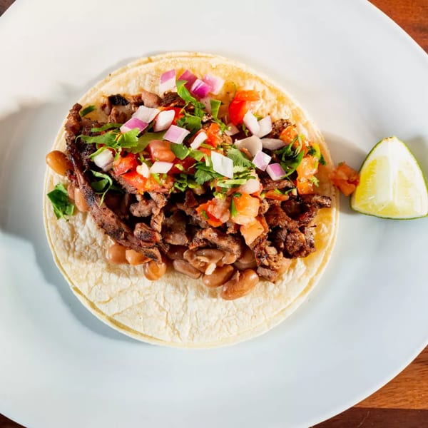 A Miguelito's Cocina Mexicana taco with meat, beans, pico de gallo, and a lime wedge.