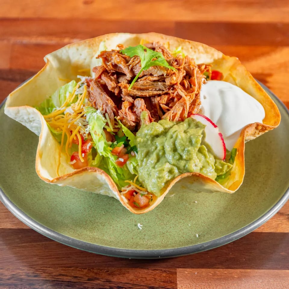 Miguelito's Cocina Mexicana taco salad with shredded meat, guacamole, and sour cream in a crispy shell.