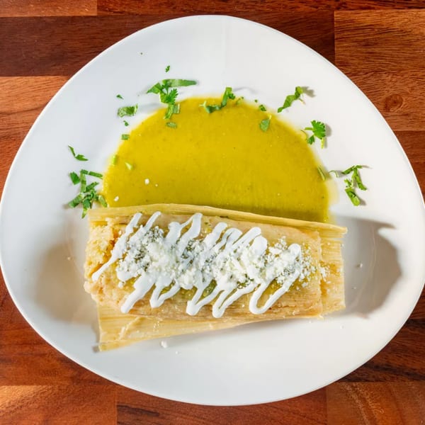 Miguelito's Cocina Mexicana tamale with green sauce, sour cream, and crumbled cheese on a white plate.