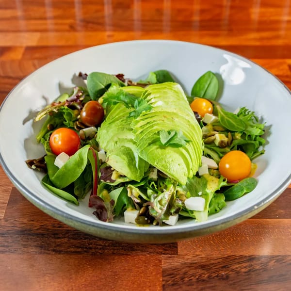 Fresh Mexican salad with sliced avocado, mixed greens, cherry tomatoes, and cheese in a white bowl.