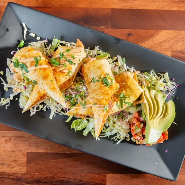 Crispy Mexican flautas drizzled with sauce, served on a bed of shredded lettuce with avocado and salsa.