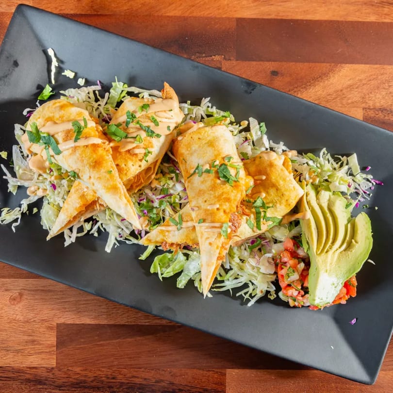 Crispy Mexican flautas drizzled with sauce, served on a bed of shredded lettuce with avocado and salsa.