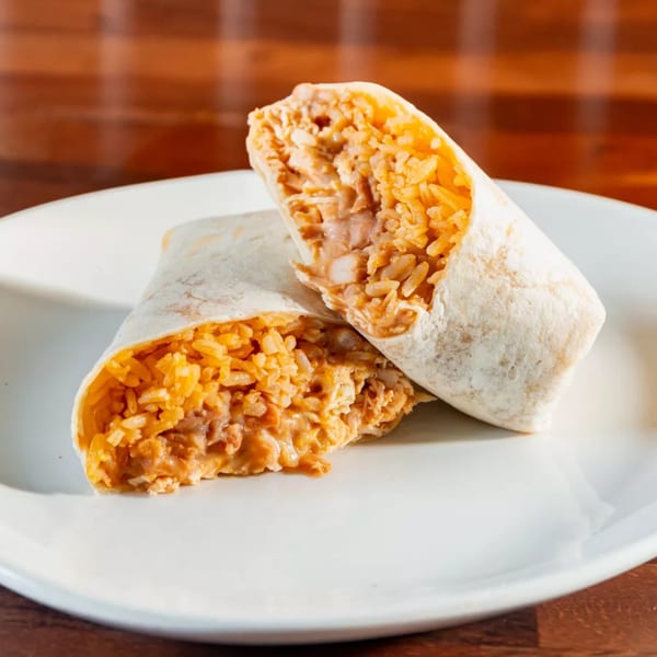 Two halves of a Miguelito's Cocina Mexicana burrito, filled with rice and beans, on a white plate.