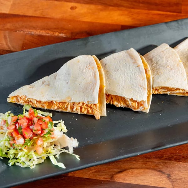 Chicken quesadillas with shredded lettuce and pico de gallo on a black rectangular plate.