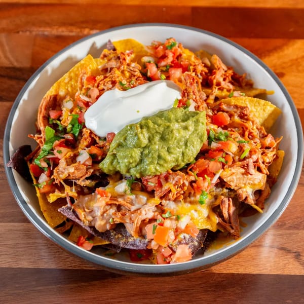 A bowl of Miguelito's Cocina Mexicana nachos with shredded chicken, pico de gallo, sour cream, and guacamole.