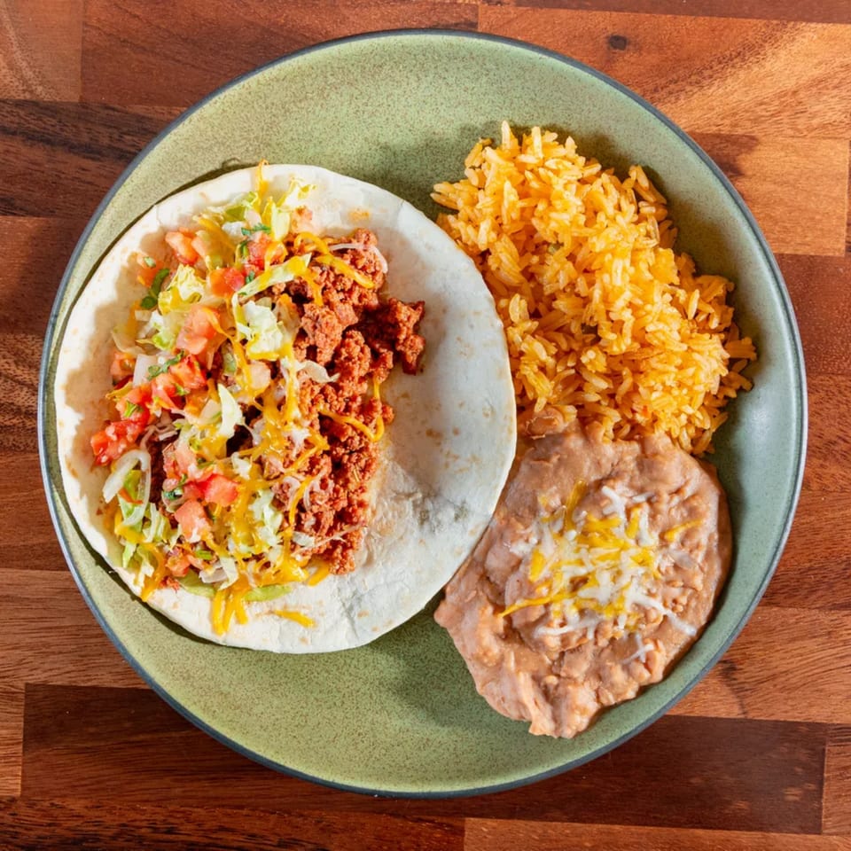 A Miguelito's Cocina Mexicana taco with rice and refried beans on a green plate.