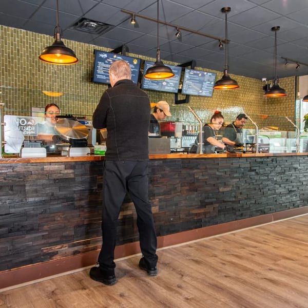 Customer ordering at Miguelito's Cocina Mexicana counter with staff preparing food behind a glass partition.