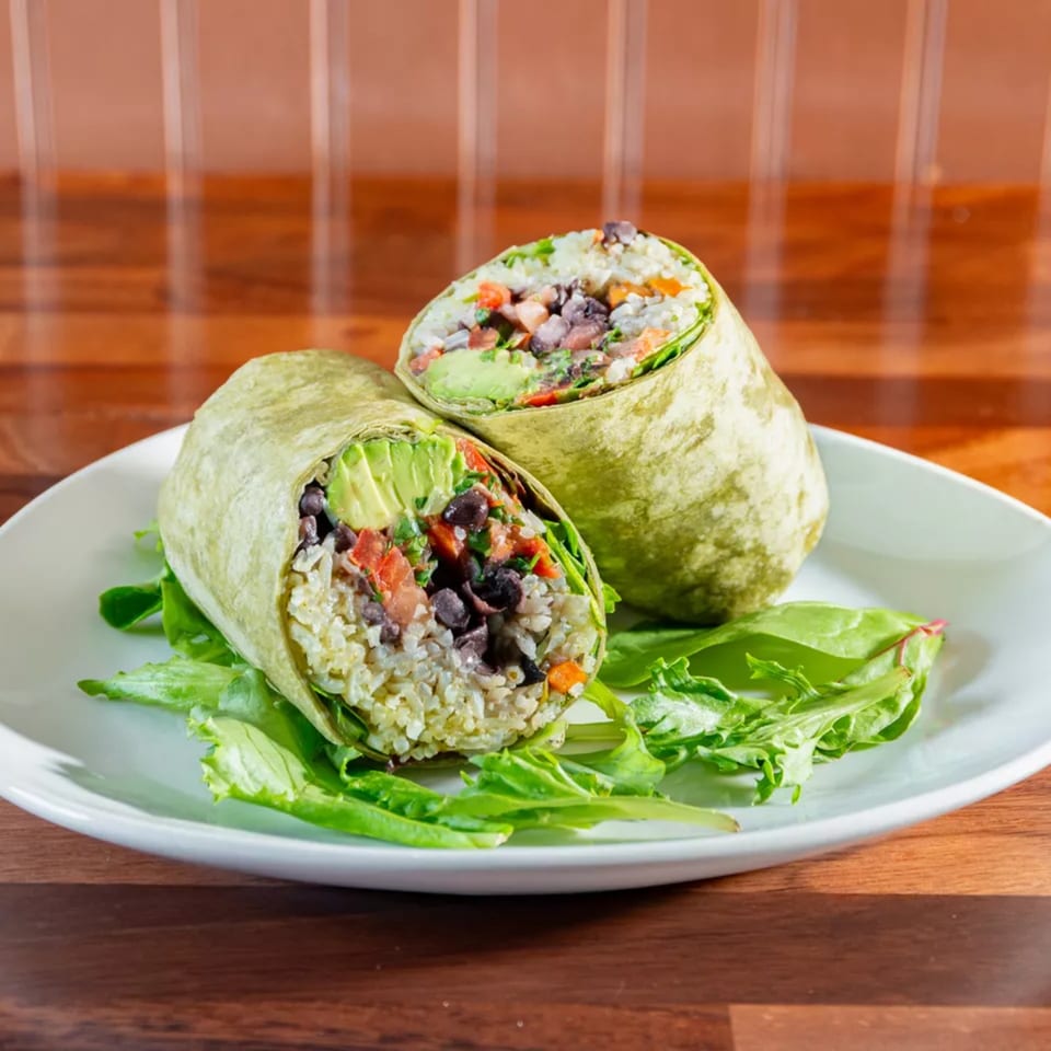 Two Miguelito's Cocina Mexicana burritos, cut in half, revealing rice, black beans, avocado, and salsa.