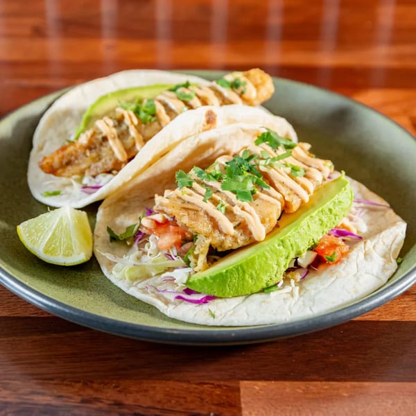 Two Miguelito's Cocina Mexicana fish tacos with avocado, cilantro, and a lime wedge.