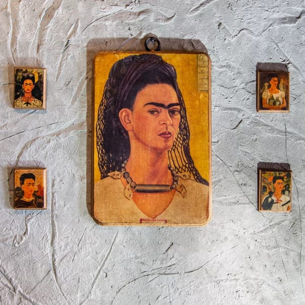 A large Frida Kahlo portrait hangs on a textured white wall, surrounded by four smaller portraits.