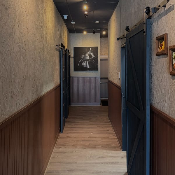 A long, narrow hallway with textured walls, dark wood wainscoting, and black barn doors.